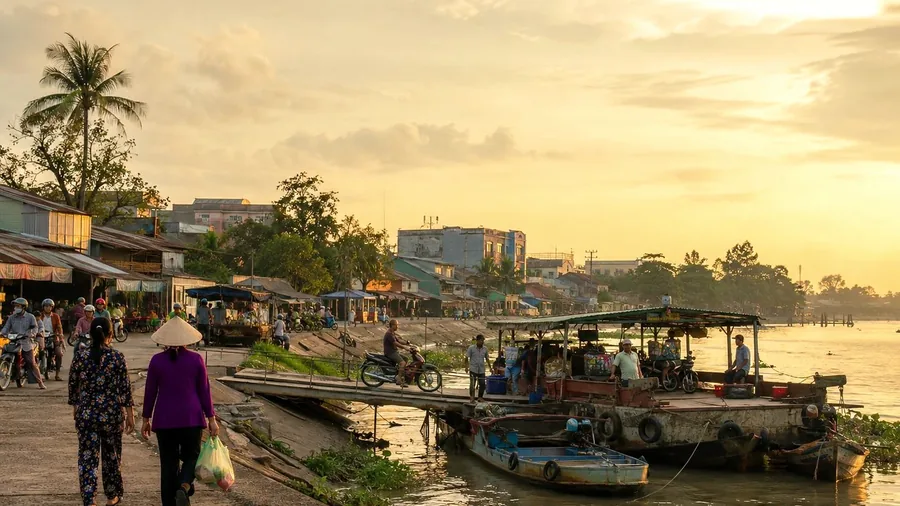 A small riverside town in the Mekong Delta at golden hour, with boats and local movement